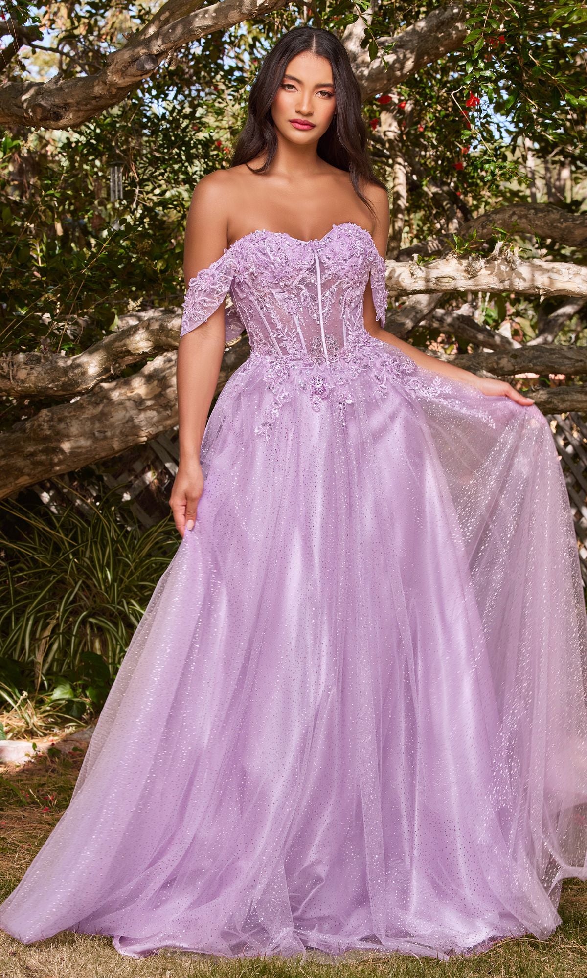 Woman standing outdoors in the Off-Shoulder Long Glitter A-Line Prom Dress CD0198, featuring a corset-style bodice, tulle skirt, and embroidered lace details, while holding one side of her gown.